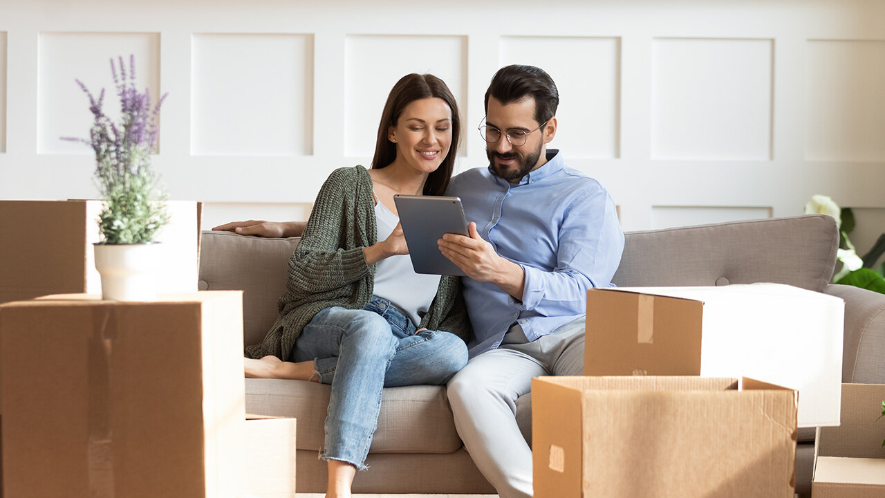 Couple sur un canapé utilisant une tablette, entouré de cartons de déménagement